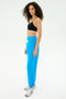 A woman stands sideways against a white background wearing a black spandex sports bra, silver athletic sneakers, and SPLITS59's Andie Oversized Fleece Sweatpant in Riviera with a white drawstring.