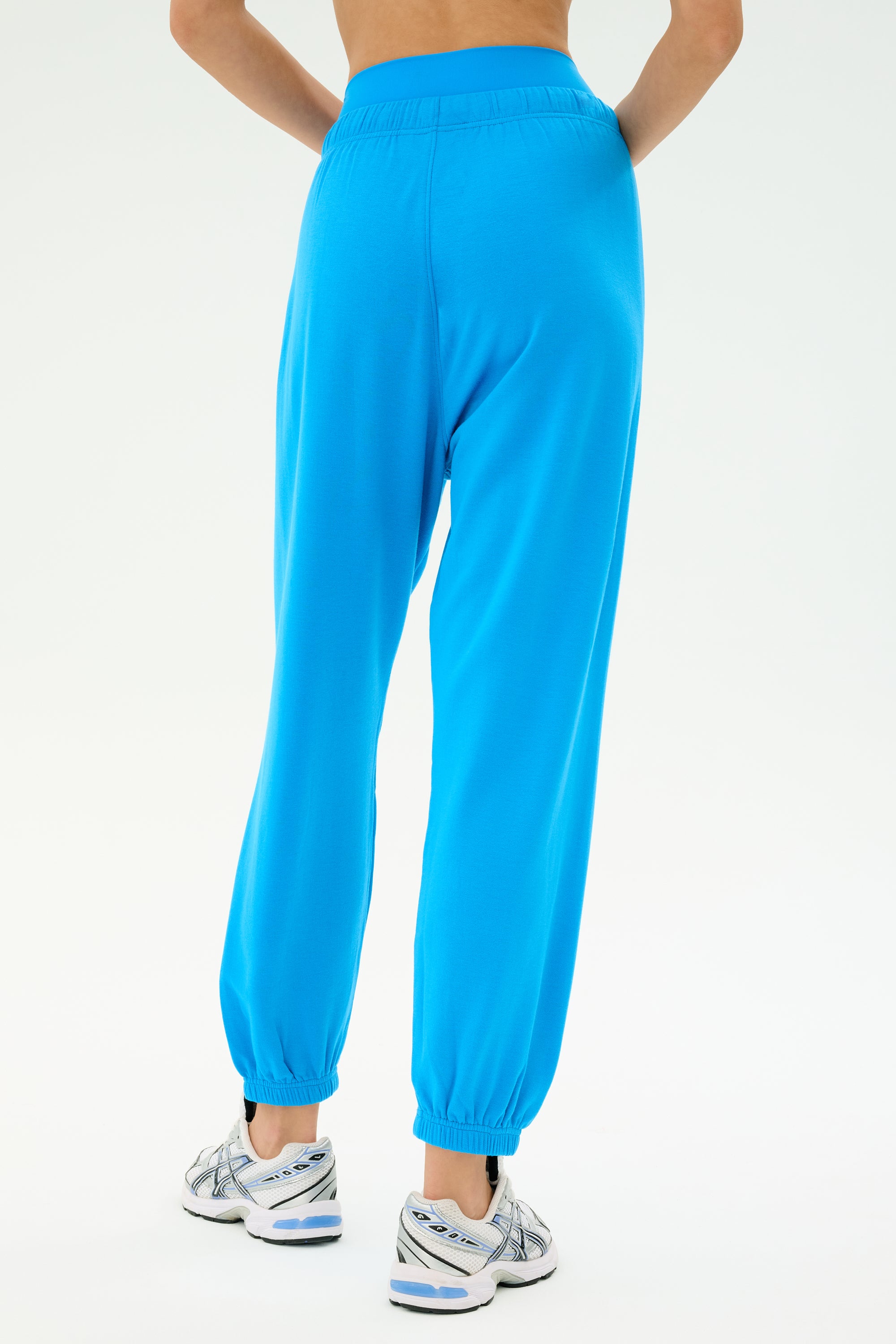 Model wearing SPLITS59's Andie Oversized Fleece Sweatpant in bright blue, paired with white athletic shoes, shown from the back against a plain light background.