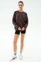 A woman stands facing forward against a white background, wearing the SPLITS59 Andie Oversized Fleece Sweatshirt in Dark Chocolate with black shorts, white socks with black stripes, and white sneakers.