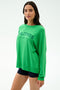 A woman wears the SPLITS59 Andie Oversized Fleece Varsity Graphic Sweatshirt in Grass/Splits59 Los Angeles, paired with black shorts, standing against a plain light background.