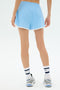 A person faces away, wearing SPLITS59 Megan Woven Nylon Run Short in Skylight, white socks with blue stripes, and gray running shoes against a plain light background.