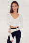 Front view of woman with dark straight hair wearing cropped white four buttoned long sleeve cardigan with thumbholes and dark blue wide bottom leggings