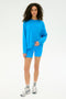 A person stands facing forward in the Andie Fleece Sweatshirt - Riviera by SPLITS59 with matching blue shorts, white athletic shoes, and striped socks against a plain white background. Made in Los Angeles.