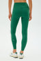 A person stands facing away in SPLITS59's Clare High Waist Rigor 7/8 leggings in Arugula/White, paired with white sneakers with a partial "550" on the leg—ideal for intense gym workouts.