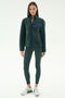 A woman wears the SPLITS59 Harris Sherpa Jacket in Military/Indigo, paired with dark green leggings and white sneakers, standing against a plain light background.