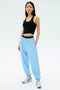 A person wearing a black sleeveless top, SPLITS59 Megan Woven Nylon Jogger in Skylight, and white sneakers stands against a plain light background.