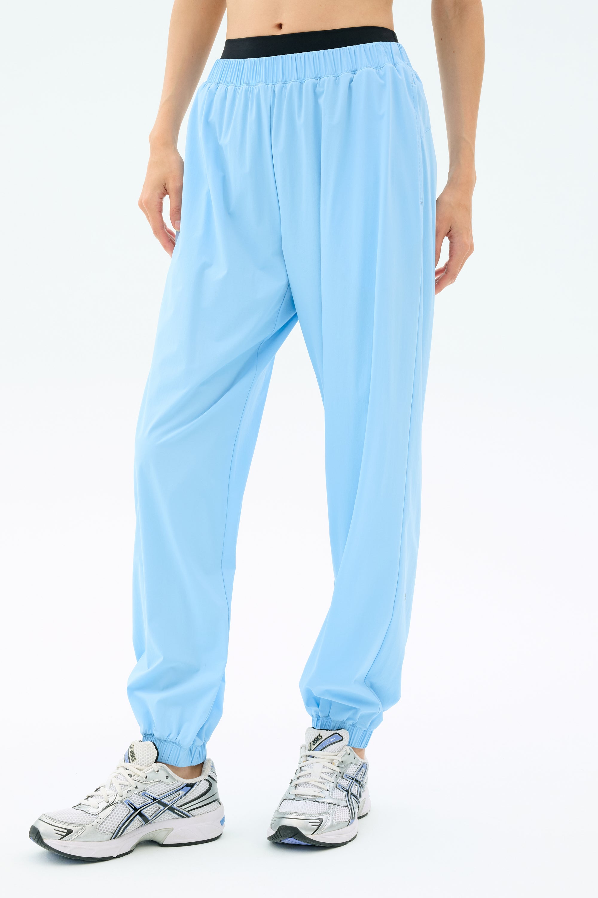 A person wears SPLITS59 Megan Woven Nylon Jogger in Skylight with white athletic shoes, standing against a plain light background. Only the lower body is visible.