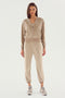 A person stands against a plain background wearing a SPLITS59 Rhys Velour Jogger - Latte tracksuit consisting of a zip-up jacket and jogger pants, paired with white sneakers. This casual wear outfit is perfect for lounging or running errands in style.