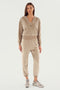 A person wearing a beige zip-up hoodie and matching Rhys Velour Jogger - Latte sweatpants from SPLITS59 stands against a plain background, with hands by their sides, looking directly at the camera. They are also wearing white sneakers, epitomizing comfort in casual wear.
