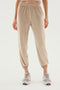 A person wearing beige Rhys Velour Jogger - Latte pants from SPLITS59 and grey sneakers stands against a plain white background, epitomizing casual wear.