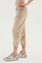 A person wearing beige Rhys Velour Jogger - Latte pants by SPLITS59 and gray New Balance sneakers stands with one leg slightly bent. The pants have an elastic waistband and cuffs, perfect for casual wear. The person's upper torso is partially visible.