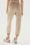 A person wearing beige Rhys Velour Jogger - Latte sweatpants and gray New Balance sneakers is standing against a white background, embodying the essence of casual wear. The focus is on the back view of the sweatpants, perfect for lounging in style.
