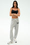 A woman stands with arms crossed, wearing a black crop top and SPLITS59 Andie Oversized Fleece Varsity 59 Sweatpant in Heather Grey with "59" on the left thigh—ideal for cool weather workouts—paired with white sneakers against a light background.