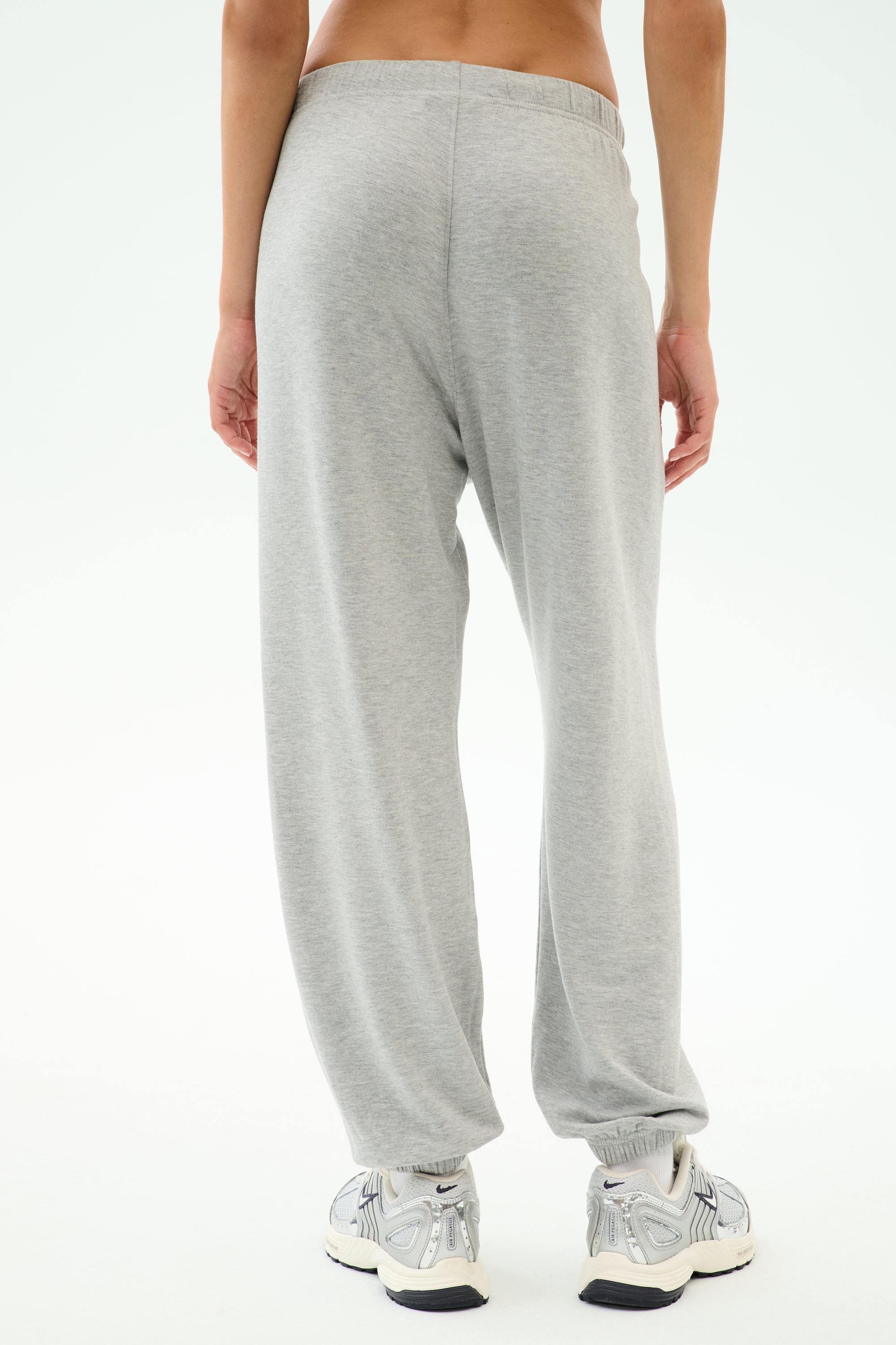A person wearing SPLITS59 Andie Oversized Fleece Varsity 59 Sweatpant in Heather Grey/59 and white sneakers, shown from the back against a plain white background—ideal for cool weather workouts.