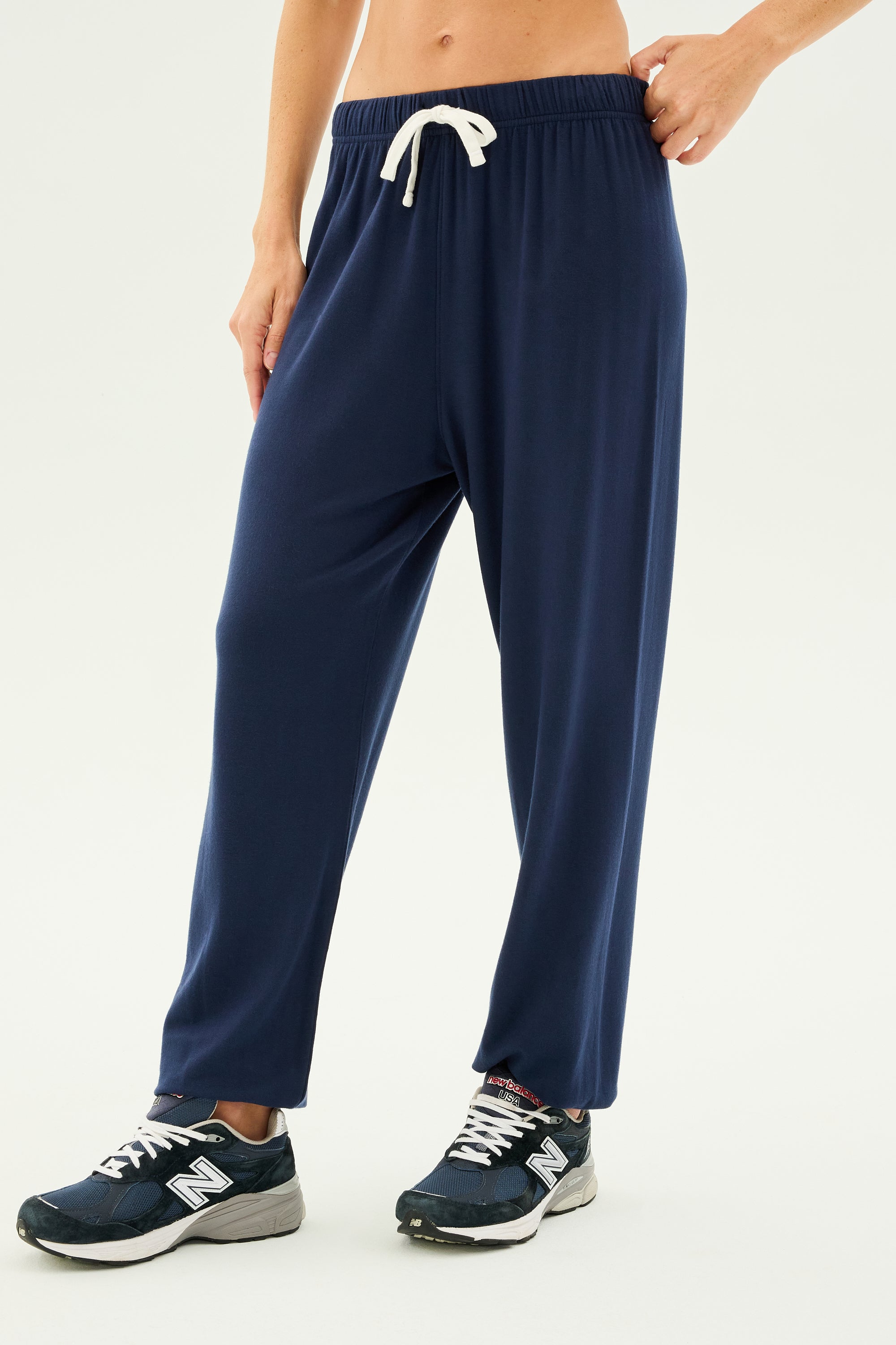 A person wearing Andie Oversized Fleece Sweatpant - Indigo by SPLITS59 and blue New Balance sneakers, perfect for cool weather workouts, stands against a plain background.