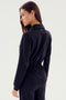 The woman with long brown hair wears a black Ollie Airweight Boiler Suit from SPLITS59, exuding modern style as she gazes over her shoulder against a plain background.
