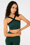 Front view of woman with dark wavy hair wearing a dark green bra with thick black cross-front neckline straps and dark green leggings.