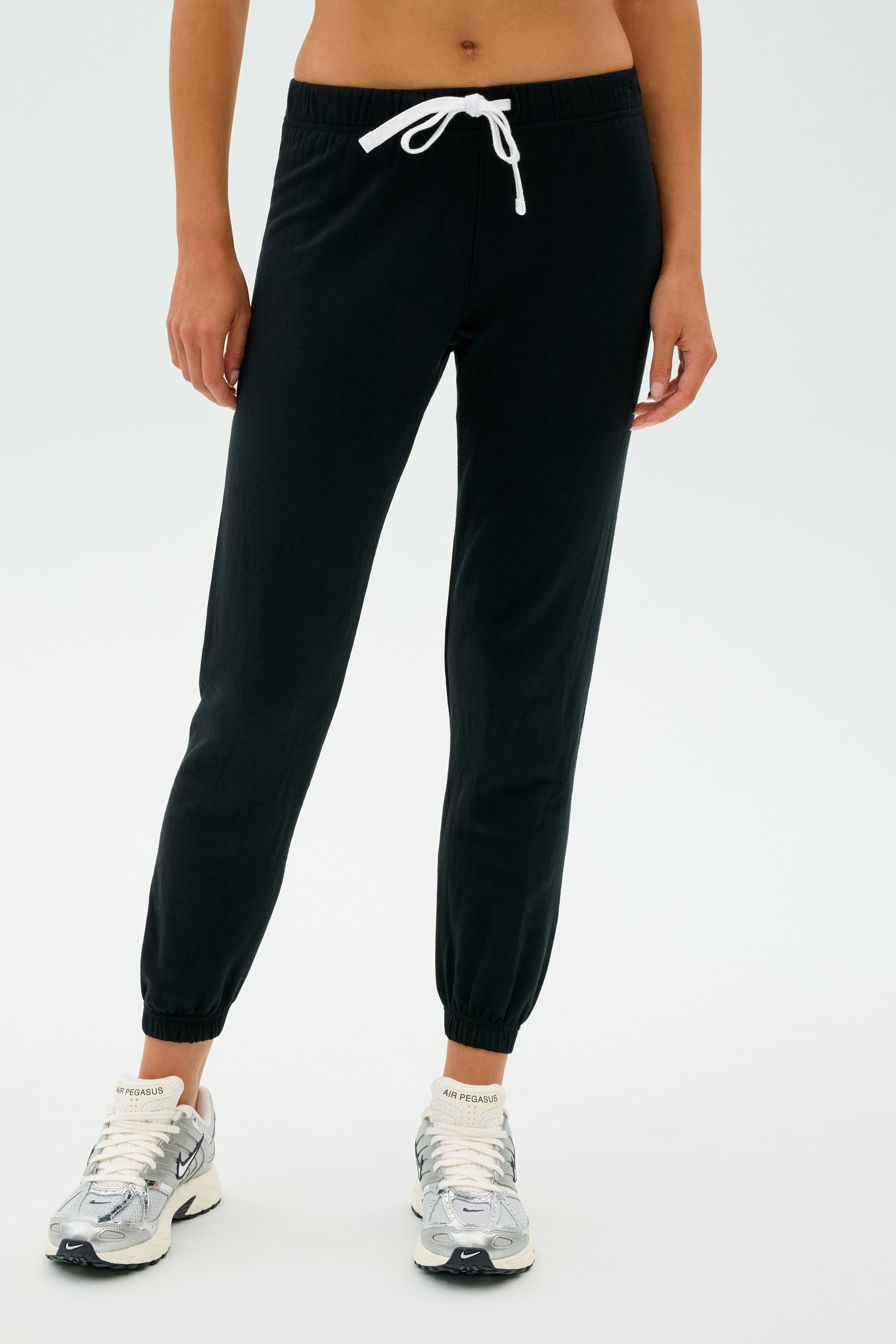 A person wearing Sonja Fleece Sweatpant - Black by SPLITS59, white sneakers, and a cropped top stands against a plain background.