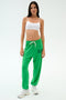 A person wears a white crop top, SPLITS59 Andie Oversized Fleece Varsity 59 Sweatpant in Grass/59, and white sneakers against a plain light background—ideal for warm weather workouts.