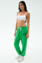 A woman stands against a white background in a white sports bra, SPLITS59 Andie Oversized Fleece Varsity 59 Sweatpant in Grass/59, and white sneakers—an ideal outfit for warm weather workouts.