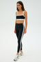 Against a plain background, a woman wears SPLITS59's Clare High Waist Rigor 7/8 leggings in Black/White with a cropped top and silver sneakers, all made from high-performance Rigor fabric.