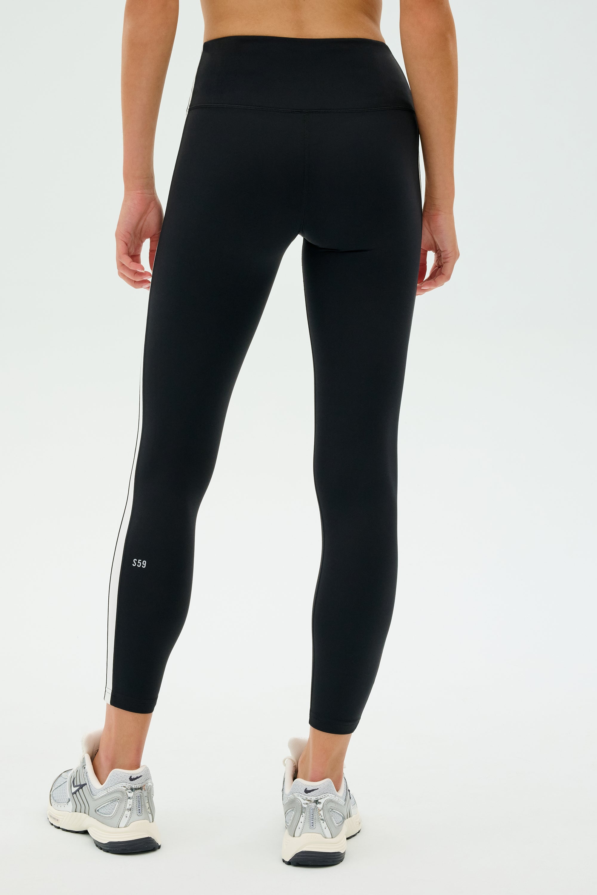 Person wearing SPLITS59 Clare High Waist Rigor 7/8 - Black/White leggings and white sneakers, standing against a plain background.