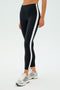 Wearing SPLITS59's Clare High Waist Rigor 7/8 leggings in Black/White with a white stripe, paired with silver running shoes, a person stands ready for high-performance gym workouts against a plain background, poised to tackle any challenge.