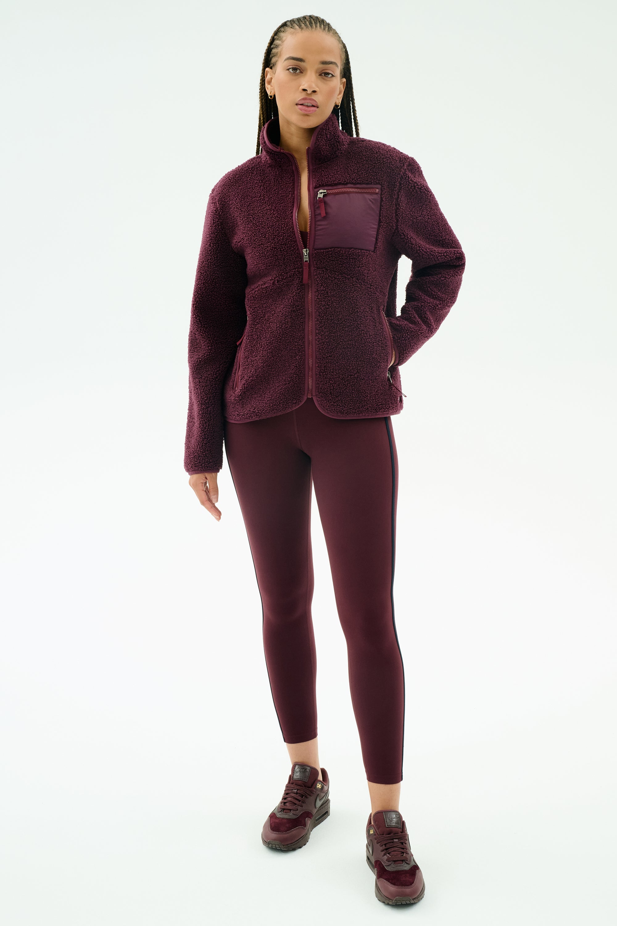 A woman wears the SPLITS59 Harris Sherpa Jacket in Dark Cherry, styled with matching leggings and sneakers, standing against a plain white background.