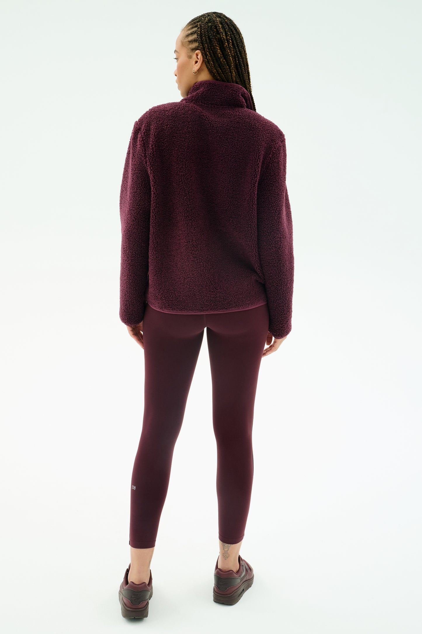 A person stands facing away against a white background, wearing SPLITS59's Harris Sherpa Jacket in Dark Cherry, paired with matching leggings and sneakers.