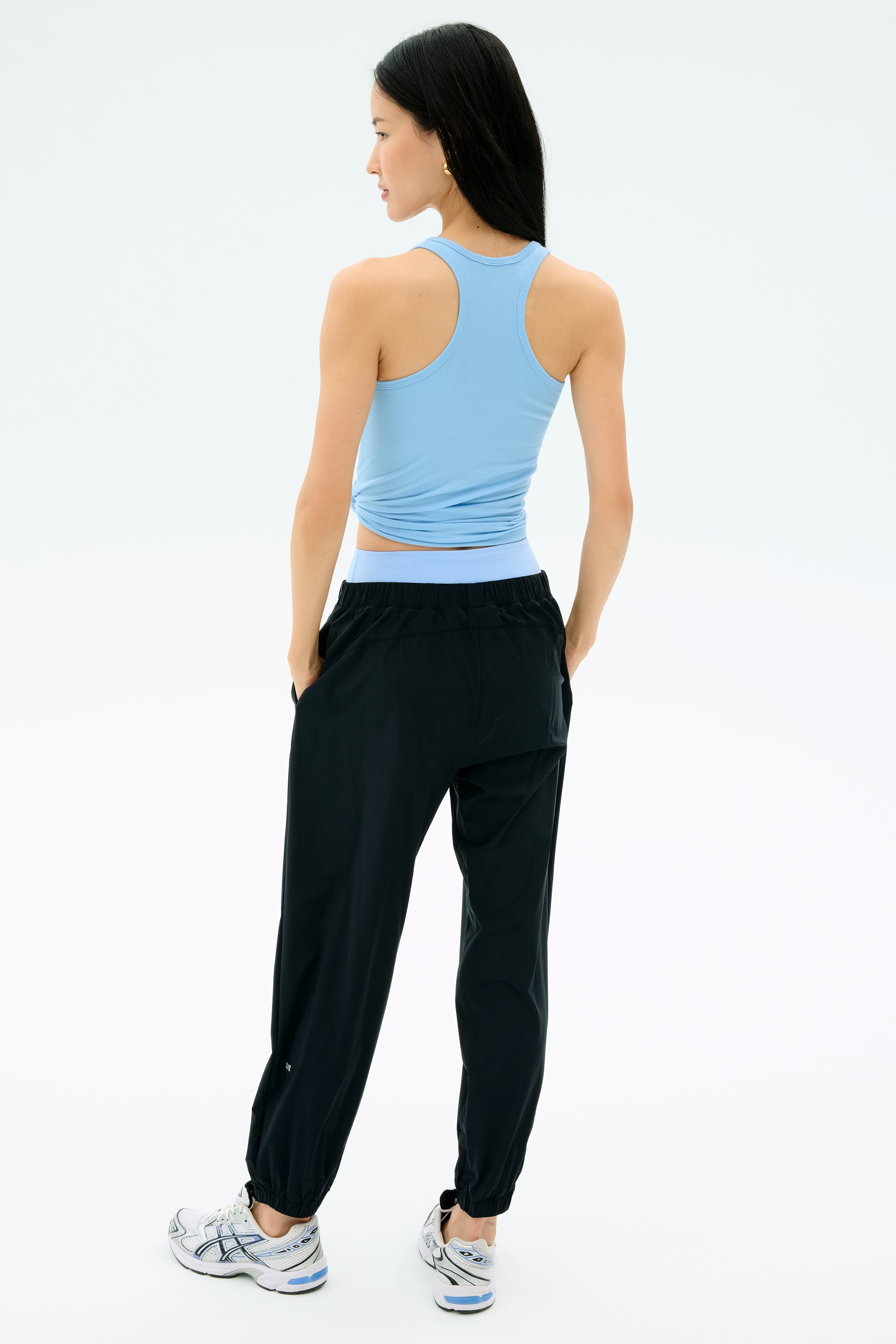 A person faces away, wearing the SPLITS59 Ashby Rib Tank in Skylight, paired with black joggers and white athletic shoes against a plain light background.