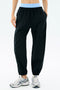 A person wearing the SPLITS59 Megan Woven Nylon Jogger in black with a blue waistband and white athletic shoes stands against a light background.