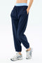 Model wears SPLITS59 Megan Woven Nylon Jogger in Indigo, featuring a light blue elastic waistband and relaxed fit, paired with white athletic sneakers. Hands in pockets, standing against a plain background.