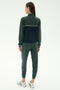 A person faces away from the camera in SPLITS59’s Millie Airweight Half Zip in Military/Indigo, crafted from soft spandex, paired with white sneakers against a plain light background.