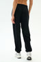 A person wears SPLITS59’s Andie Oversized Fleece Varsity 59 Sweatpant in Black/59 with white sneakers, standing on a white background and facing away from the camera—perfect for cool weather workouts.