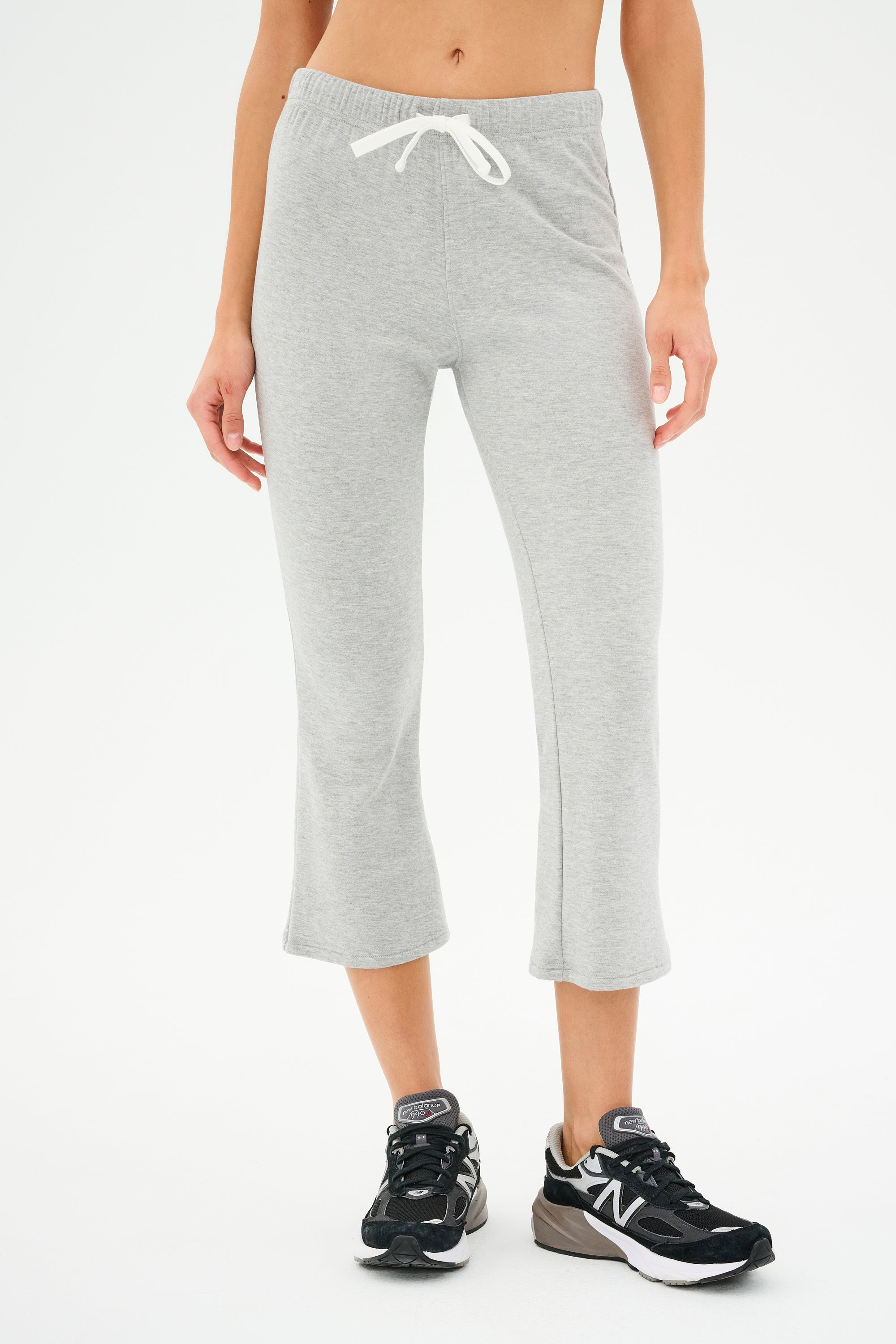 A person wearing SPLITS59's Brooks Fleece Cropped Flare in Heather Grey and black sneakers stands against a plain background, exuding comfy casual chic.