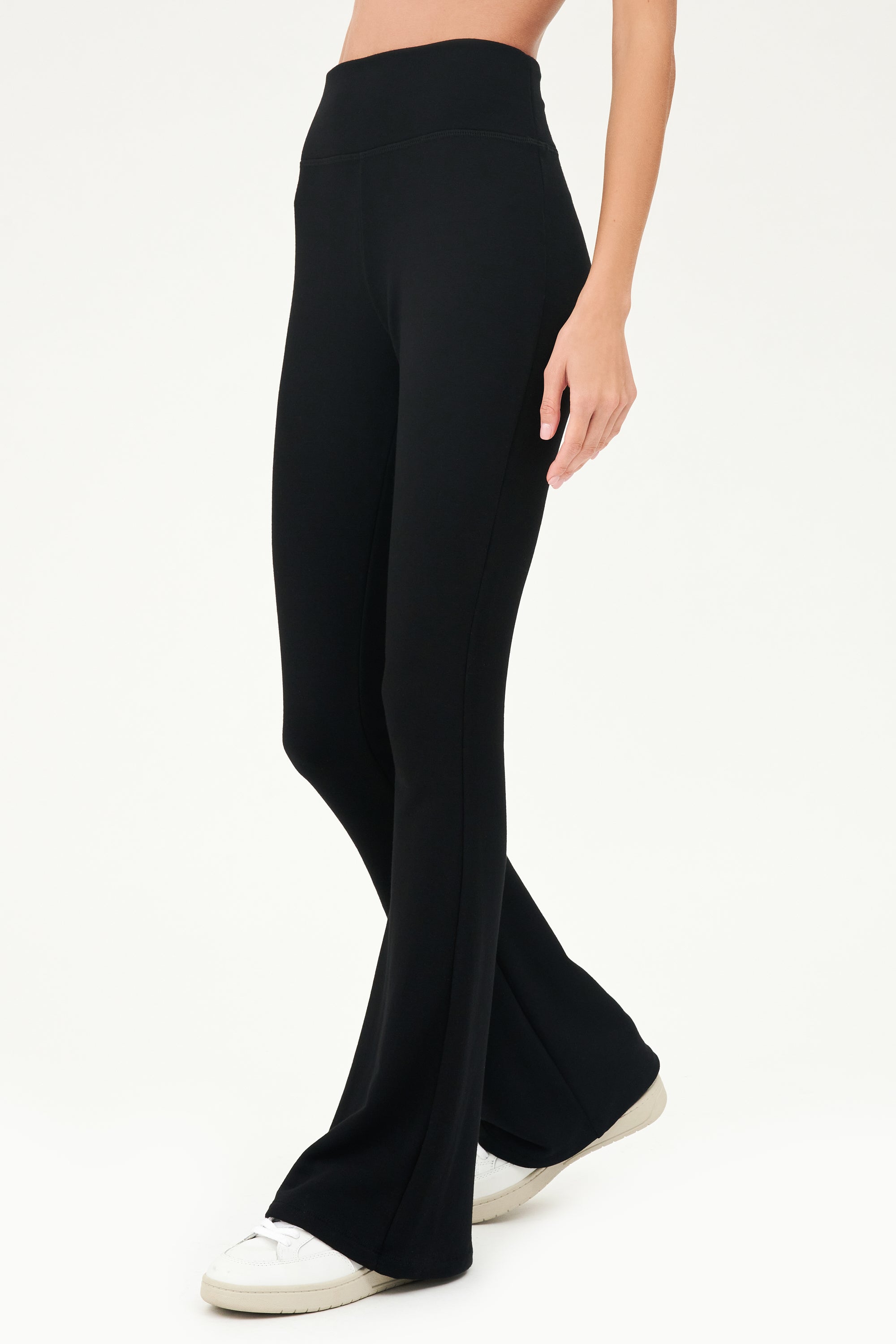 A woman wearing the SPLITS59 Raquel Fleece Flare - Black leggings and a white top.