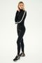 A person wearing the Jackson Rib Full Length Turtleneck in Black/White by SPLITS59, paired with black sneakers featuring white soles designed for running, stands against a plain background, looking to one side.