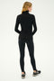 A person stands facing away, adorned in a black Jackson Rib Full Length Turtleneck from SPLITS59 and black leggings, prepared for yoga.