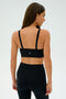 A woman in black athletic wear, wearing the SPLITS59 Monah Rigor Bra - Black, turns away, highlighting the sleek design of her sports bra and leggings against a plain backdrop—ideal for intense gym workouts.