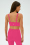 A woman faces away, wearing a matching berry Monah Rigor Bra by SPLITS59 and high-waisted leggings—an ideal gym look—against a plain light background.