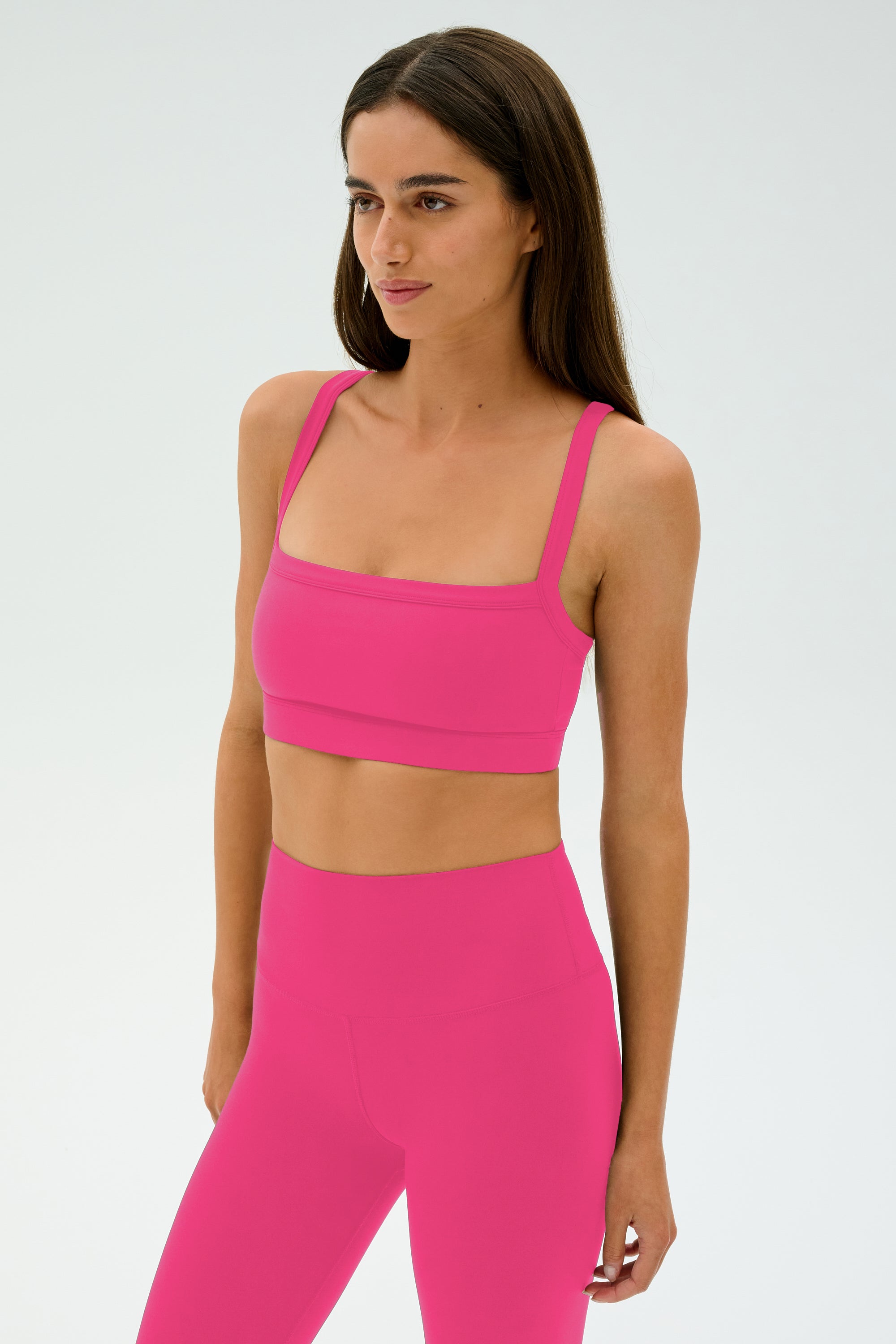 A woman wears the SPLITS59 Monah Rigor Bra - Berry with matching high-waisted leggings, ideal for gym or workout sessions, set against a plain light background.