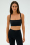 A woman wearing a SPLITS59 Monah Rigor Bra - Black and leggings stands against a plain background, epitomizing gym workouts as she gazes directly at the camera.