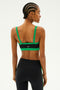 A woman with braided hair is seen from the back wearing the Monah Rigor Bra in black/grass by SPLITS59, paired with black leggings, against a light background.