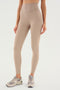 A person wearing beige Airweight Super High Waist 7/8 - Latte leggings from SPLITS59 and gray sneakers stands against a white background. The image is cropped from the shoulders down.