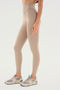 A person wearing SPLITS59 Airweight Super High Waist 7/8 - Latte leggings and gray sneakers stands against a plain white background.
