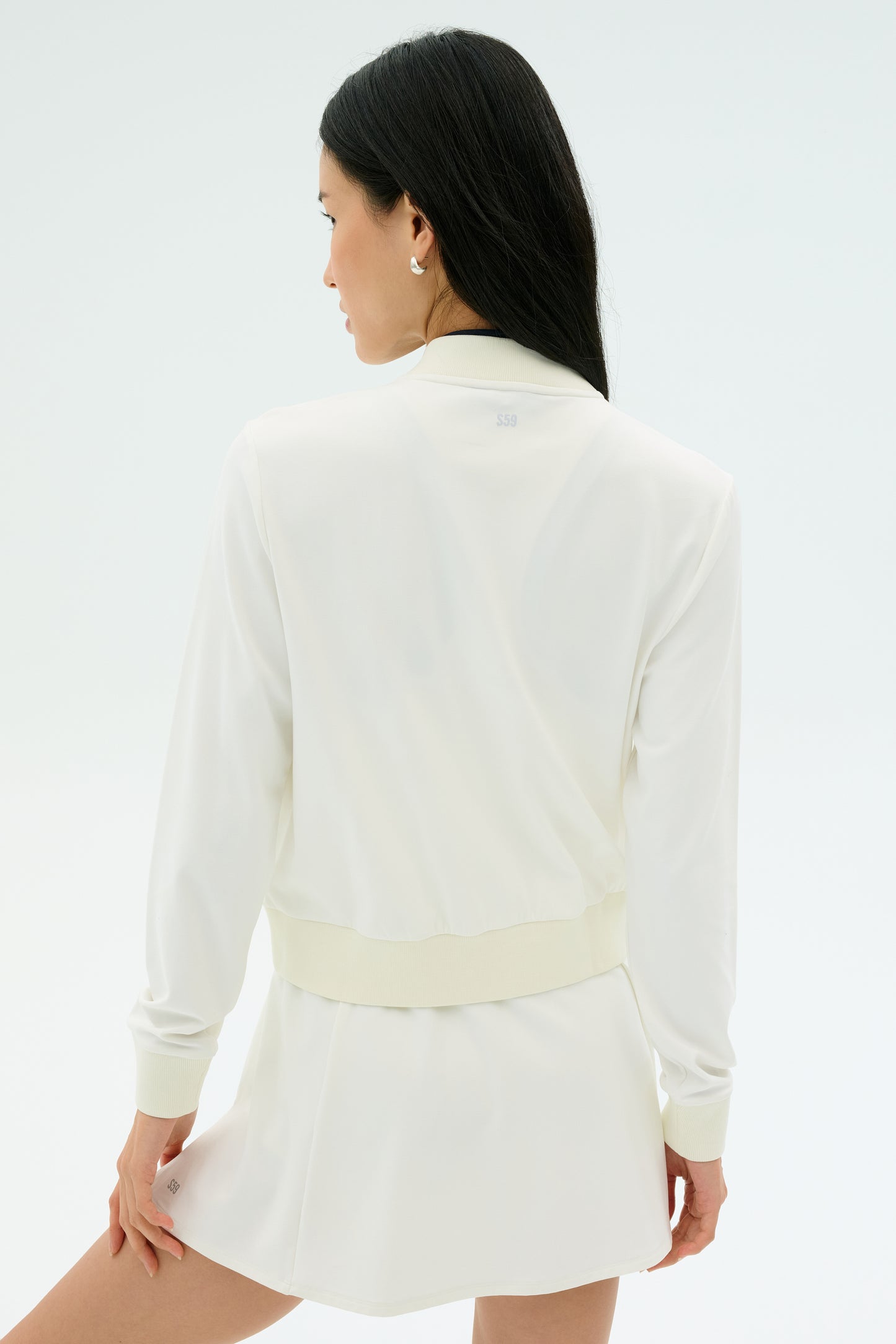 A woman with long dark hair is seen from the back wearing the SPLITS59 Airweight Bomber Jacket in white against a light background.