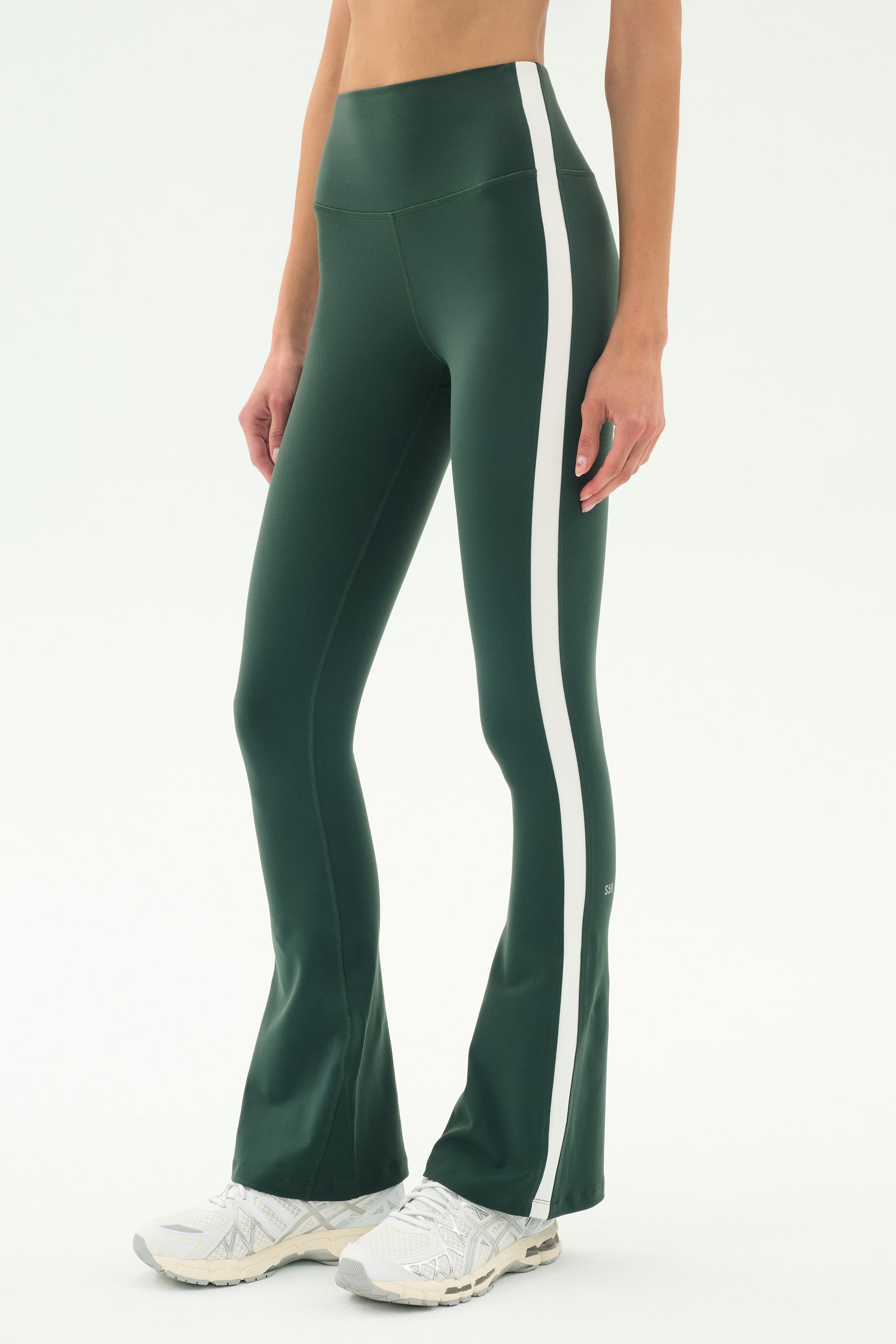 A person wearing SPLITS59's Raquel High Waist Flared Legging in Military/White and white sneakers stands against a plain background.