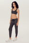 Full side view of girl wearing dark grey sweatpants with black tie around waistband and a dark grey sports bra with white shoes