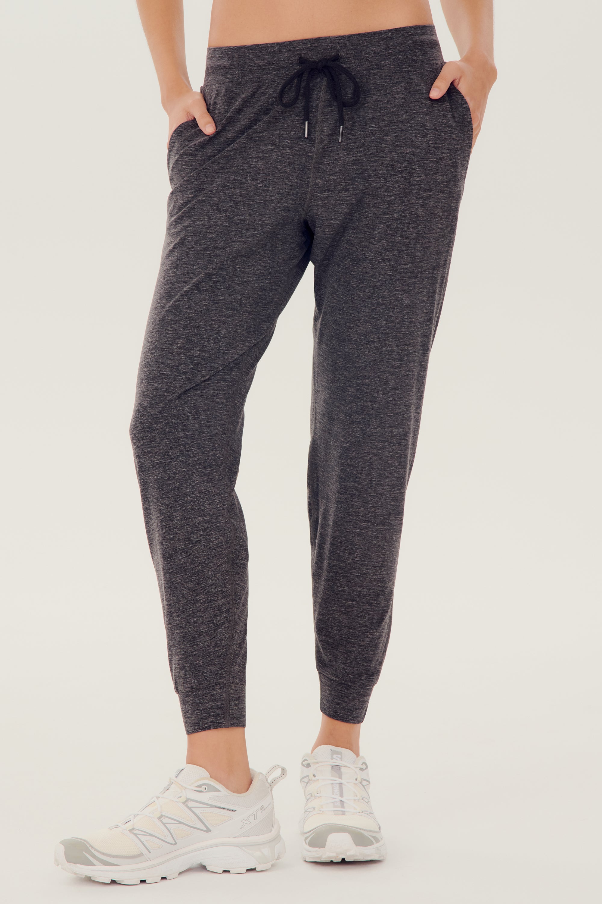 Front view of girl wearing dark grey sweatpants with black tie around waistband with white shoes