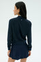 A woman faces away from the camera, wearing the SPLITS59 Airweight Bomber Jacket in Indigo, paired with a matching skirt against a plain light background.